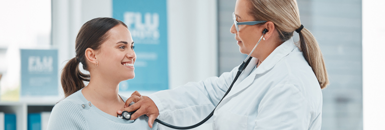 A female doctor is seen holding a stethoscope to a woman's chest on a hospital floor.